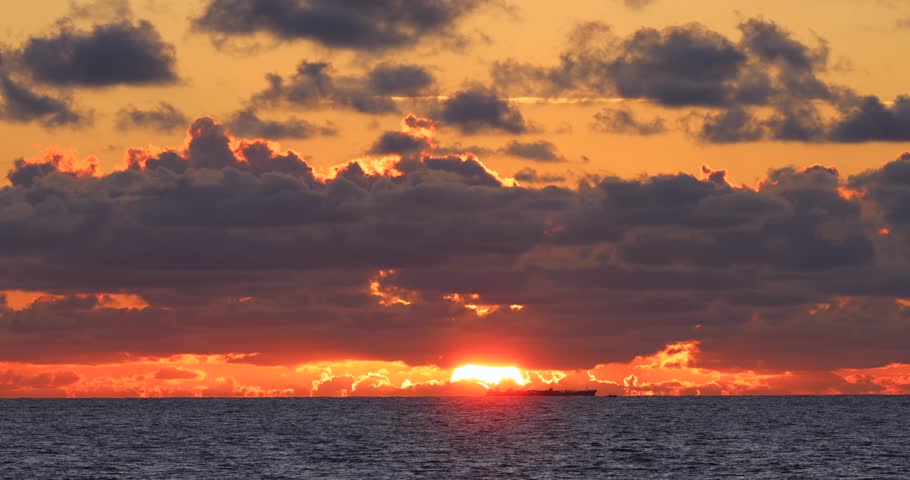 The ship sails in the ocean against the backdrop of the rising sun under the clouds