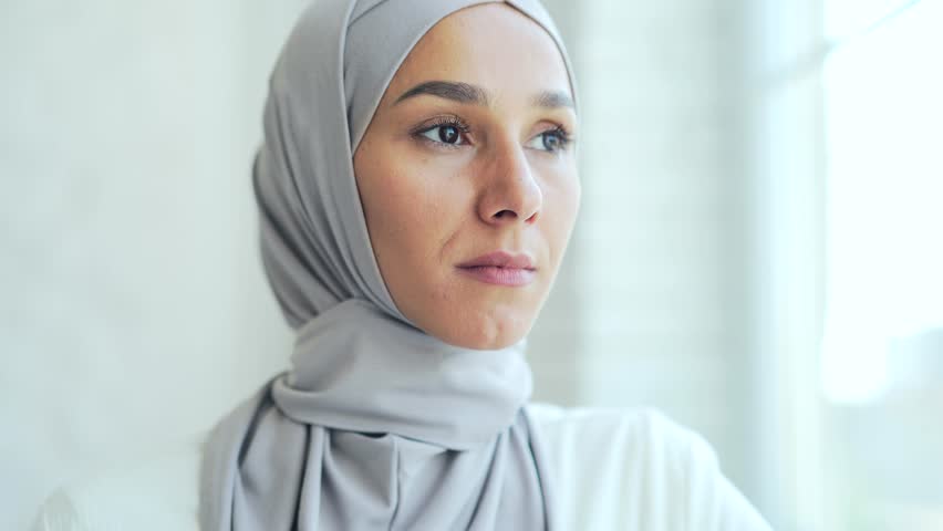 closeup portrait of a pretty young Muslim woman in hijab standing and smiling indoors at home Headshot of an Islamic happy female girl looking at camera on a light room background close up Royalty-Free Stock Footage #1098825447