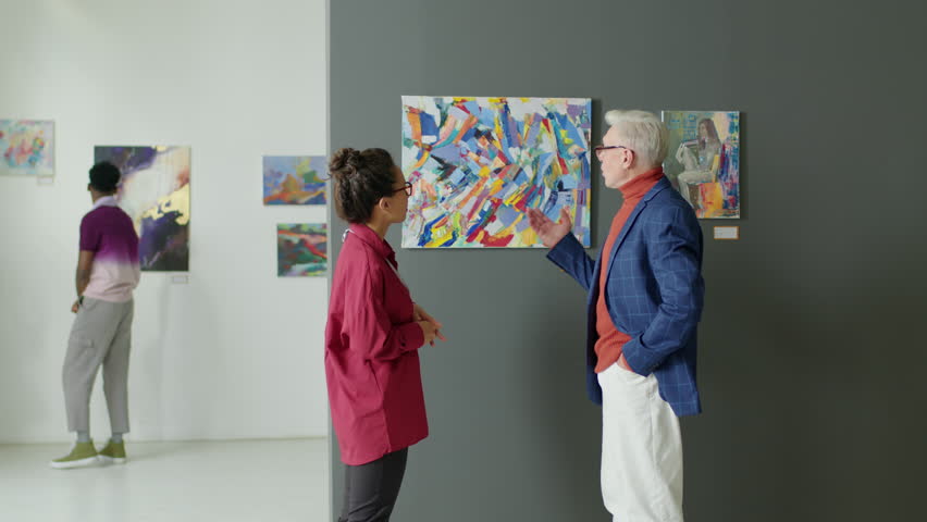 Mature man and young woman discussing abstract painting while visiting contemporary art gallery Royalty-Free Stock Footage #1098825929