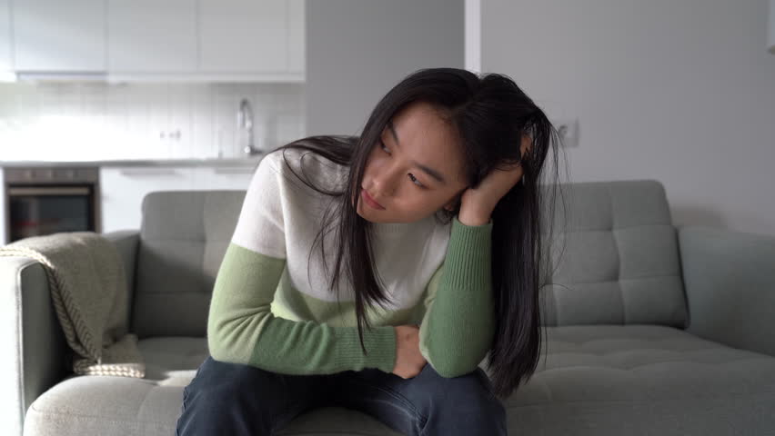 Depression and anxiety. Depressed young Asian woman feeling sad after loss, coping with breakup or divorce, anxious unhappy Korean girl sitting on sofa at home. Mental illness and grief concept | Shutterstock HD Video #1098825987