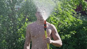 Young man watering lawn and plants in garden using hosepipe, spraing water up for better distribution, close up video