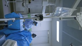 Vertical Screen: Intravenous drip on the stand in surgical theatre. Medical team performing surgery at backdrop.