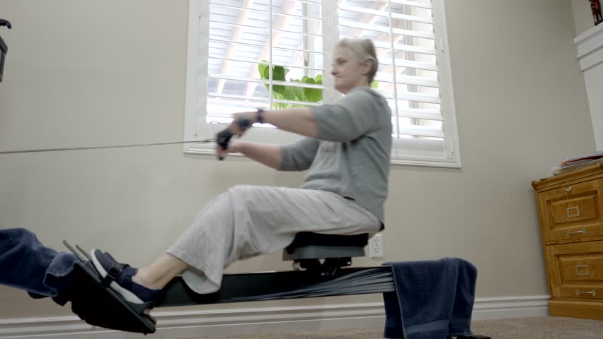 Senior woman exercising on a rowing machine - low angle sliding