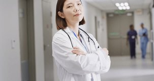Video portrait of smiling asian female doctor standing in busy hospital corridor, copy space. Hospital, medical and healthcare services.