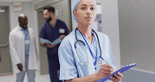 Video portrait of biracial female doctor in surgical cap smiling in hospital corridor, copy space. Hospital, medical and healthcare services.