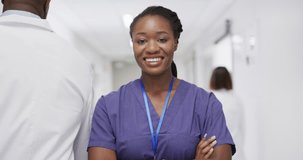 Video portrait of african american female doctor smiling in busy hospital corridor, copy space. Hospital, medical and healthcare services.