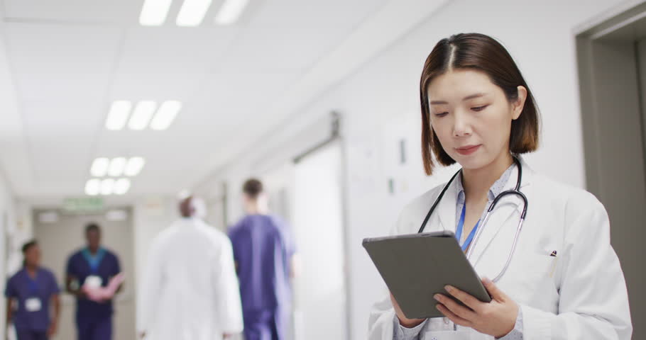 Video portrait of smiling asian female doctor with tablet in hospital corridor, with copy space. Hospital, medical and healthcare services. | Shutterstock HD Video #1098835221