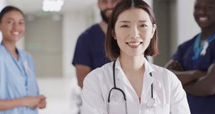 Video portrait of smiling asian female doctor with cancer ribbon in hospital corridor, copy space. Hospital, medical and healthcare services.
