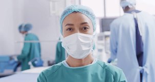 Video portrait of biracial female surgeon in face mask in operating theatre, with copy space. Hospital, medical and healthcare services.