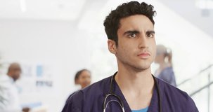 Video of serious biracial male doctor walking in busy hospital corridor, with copy space. Hospital, medical and healthcare services.