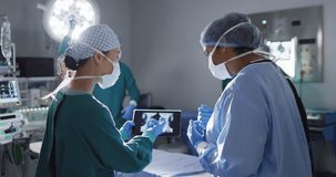 Video of two diverse female surgeons discussing x-ray on tablet in operating theatre. Hospital, medical and healthcare services.