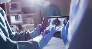 Video of midsection of two gloved surgeons discussing x-ray on tablet in operating theatre. Hospital, medical and healthcare services.
