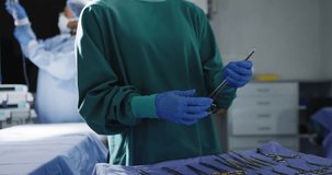 Video of asian female surgeon checking instruments looks to camera in operating theatre, copy space. Hospital, medical and healthcare services.