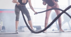 Video of diverse female fitness trainer encouraging woman battling ropes working out at a gym. Exercise, fitness and healthy lifestyle.