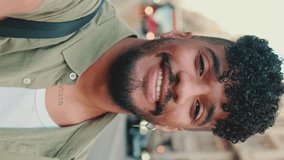 VERTICAL VIDEO: Young happy man with beard, dressed in an olive-colored shirt, stands next to the road, smiles and takes selfie