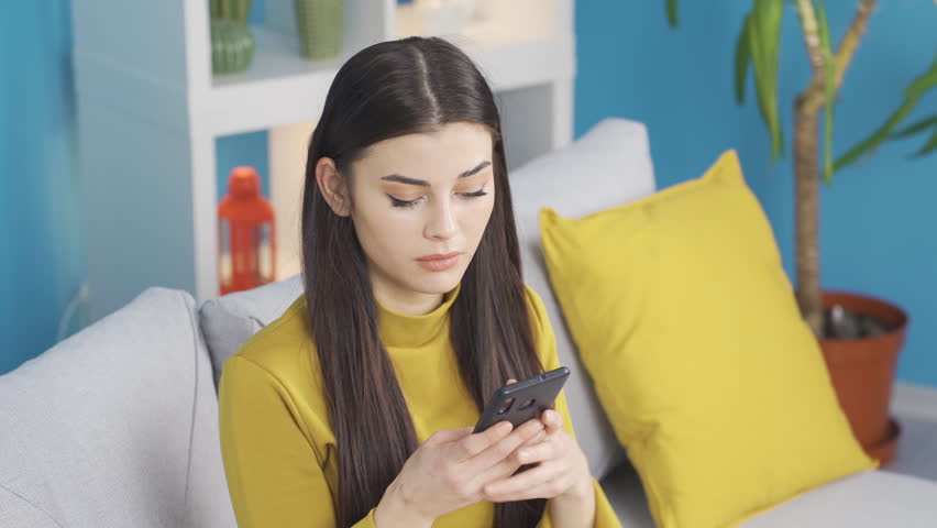 Beautiful hammering young woman sitting on sofa at home looking at her phone, texting.
Pretty young woman texting on phone, feeling confused and distracted. Messaging, arguing with your lover.
 | Shutterstock HD Video #1098842299