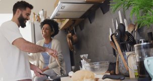 Video of happy diverse couple laughing and cooking breakfast in kitchen, with copy space. Happiness, inclusivity, free time, togetherness and domestic life.