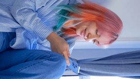 Happy young woman scrolling mobile phone app at home. Cheerful female person with rainbow colored hair browsing application on modern smartphone in vertical 4k video clip