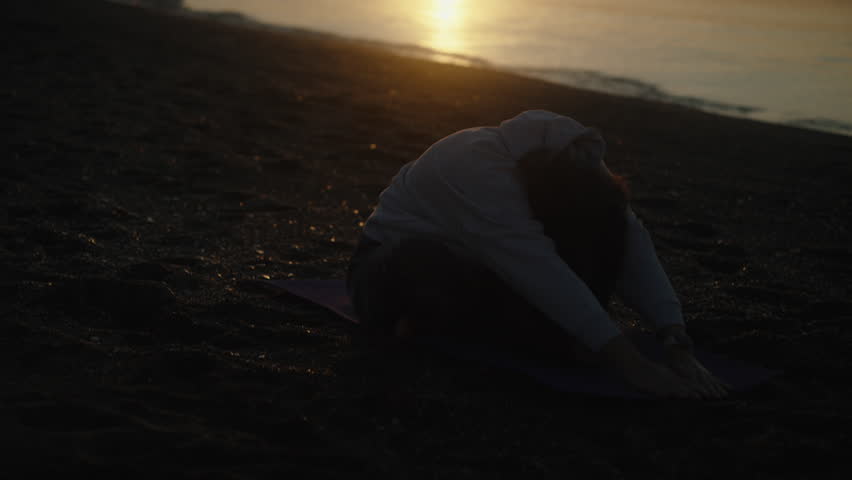 Yoga at dawn on the seashore. The girl is sitting on the rug and stretches her hands to the sun. | Shutterstock HD Video #1098849109
