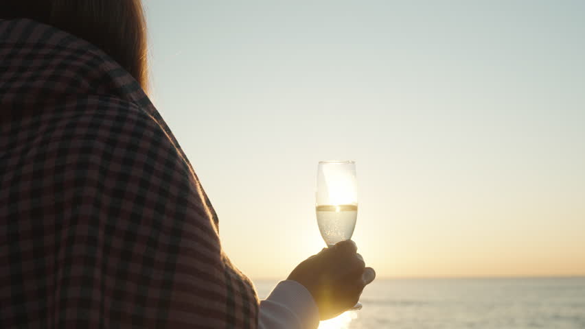 A girl wrapped in a blanket meets the Sunrise at the Sea with a glass of champagne in her hand. | Shutterstock HD Video #1098849157