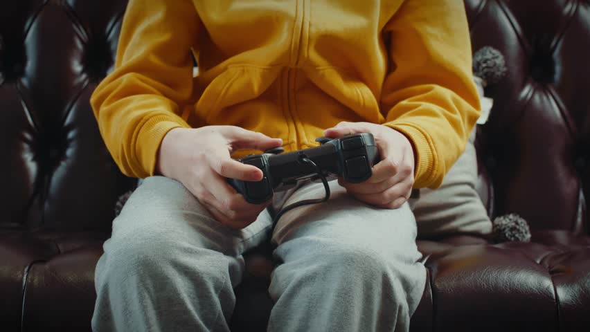 Child or boy playing video games on modern console, happy child sitting on sofa in living room, cheerful teenager using gamepad enjoying game