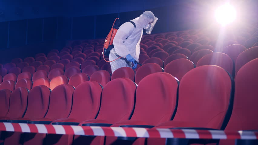 Man wearing a hazmat suit chemically disinfects a movie theater