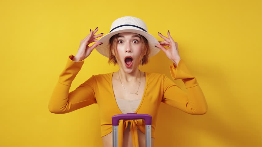 Travel excitement. Expressive woman. Vacation trip. Happy amazed lady in summer look showing overwhelmed emotion posing with suitcase on yellow background. Royalty-Free Stock Footage #1098855479