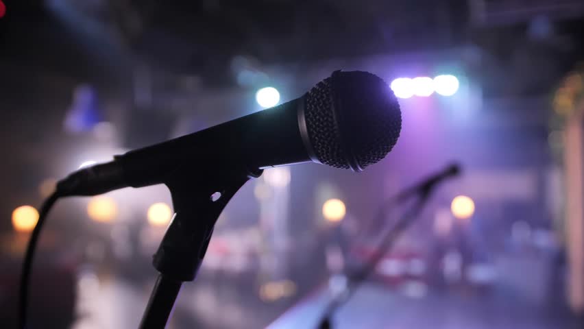 Close-up of microphone on stage against a black background with white lighting. The silhouette of the microphone in the dark. Music instrument concept.