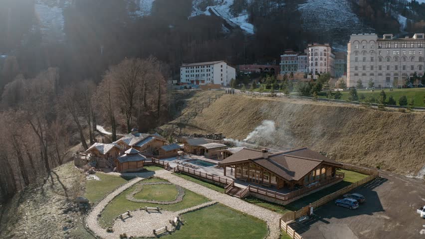 Around view wooden bathhouse at countryside city surrounded mountain snowy peaks late fall autumn aerial. Drone shot comfortable heat apartment recreation bungalow spa resort village exterior building
