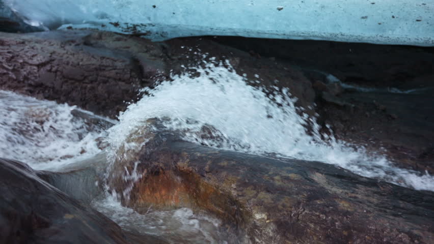 Environment preservation. Glacier meltdown in summer. Inside the glacier caves. Closeup view of the white water glacier stream flowing along the rocky mountain under the glacier ice field.