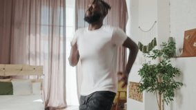 Young Beginner African American handsome man doing cardio exercise in living room at home. Attractive active male doing workout follow instruction video from online trainer on laptop computer in house