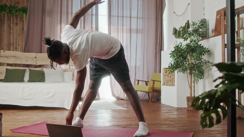 Young Beginner African American man doing gymnastics exercise on floor in living room. Attractive handsome sport male spend leisure activity time to workout for healthcare by follow online instruction Royalty-Free Stock Footage #1098861729