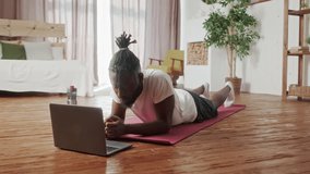 Young Beginner African American man doing cardio exercise on floor in living room. Attractive handsome sport male spend leisure activity time to workout for healthcare by follow online instruction on
