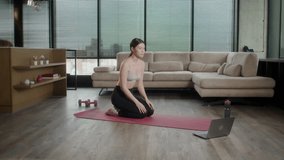 Cheerful active asian woman doing fitness at home, using laptop, watching online lessons. Positive well-fit lady in sportswear exercising during covid-19 pandemic, watching fitness videos on Internet