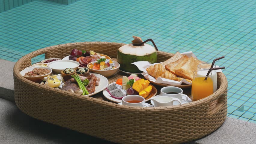 Floating breakfast tray in luxury poolside hotel. Hotel breakfast with fresh croissants, tropical fruits and juices. Luxurious travel, resort vacation, holidays in Thailand, exotic summer travel