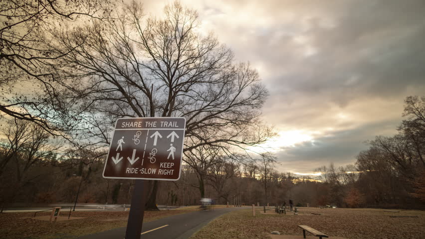 In Rock Creek Park, a time-lapse shot captures a multi-use trail sign and exercise course. In the background, blurred figures of passing people and fitness enthusiasts showcase the park