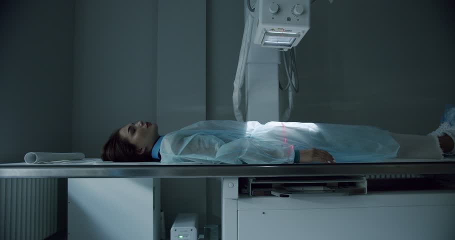 Female patient on X ray machine. Pan left and right view of woman in disposable robe lying on table during belly X ray scanning procedure in modern laboratory. | Shutterstock HD Video #1098865329