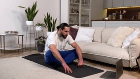 Calm mid adult man watching online video tutorial following instruction yoga breathing exercises at domestic room. Sporty male practicing pranayama by online classes on laptop sitting yoga mat at home