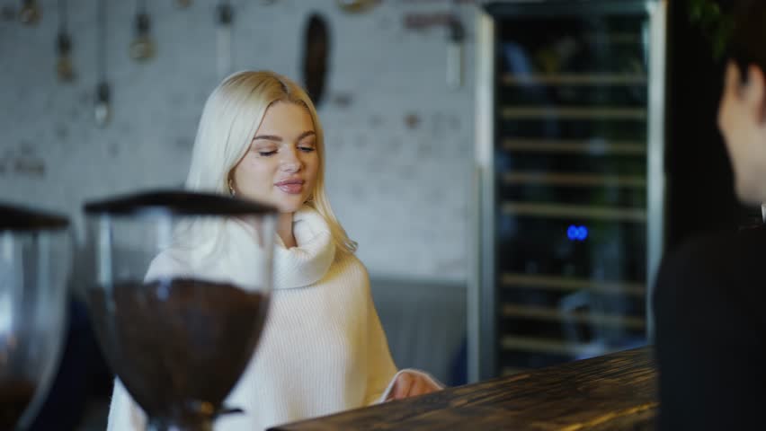 Smiling blonde girl makes order in coffee shop to bartender woman