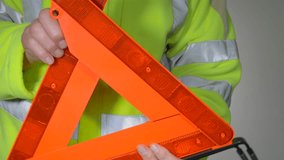 Closeup POV shot of a man wearing a fluorescent yellow, high visibility or hi vis or hi viz, fleece safety jacket, unfolding an orange, reflective warning triangle, ready for use. - Powered by Shutterstock - Get 15% off with code: PIKWIZARD15