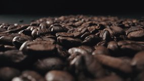 Close-up video moving away, from scattered coffee beans over black surface. Food and drink consumerism. Coffee industry. Steadicam shot. Macro 4k video footage