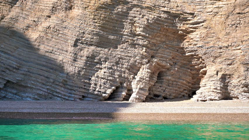 Rock geology layers visible at cliffs near Chomi or Paradise beach at Liapades, Greece, calm green sea in foreground. View from a boat
