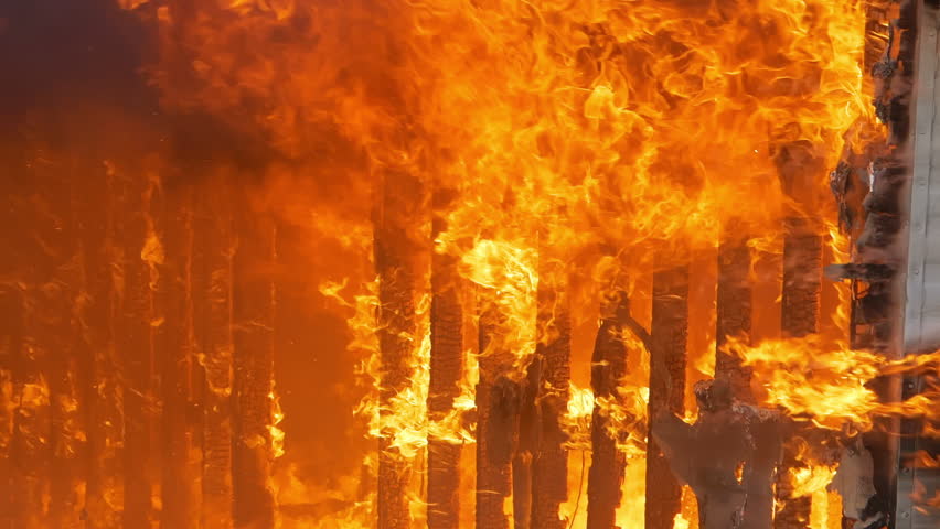 Slow motion flames engulfing a small building. House wall being burned down by a massive fire. Slow motion footage.