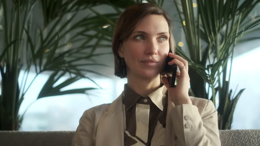 Close-up face of a confident serious business woman calling for work in a cafe using a mobile phone. A beautiful young woman with dark hair is talking on a smartphone. Close-up of a lady talking