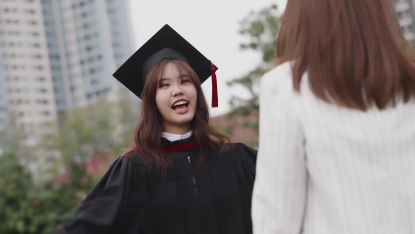 Happy Asian girl in graduation gowns with holding diploma are hugged mother by love and proud. Asian mom embraces daughter with joy on graduation day and successful. Royalty-Free Stock Footage #1098883071