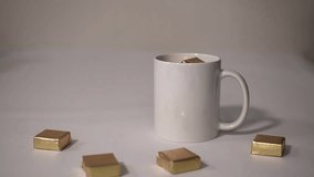 sweets in a golden wrapper fall into a white mug. High quality Full HD video recording