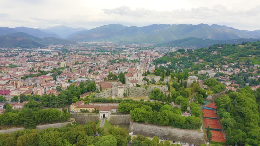 Inscription on video. Brescia, Italy. Castello di Brescia. Flight over the city in cloudy weather. Different colors letters appears behind small squares, Aerial View, Point of interest