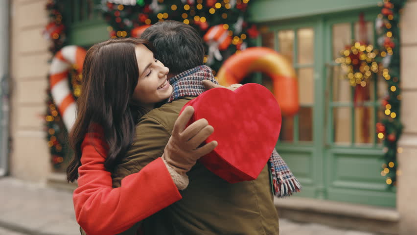 Happy couple in love. Valentines day. Romance, relationships. Husband gives his beautiful wife a red heart shaped gift. Lovey couple in love spending time together exchanging presents. Festive mood