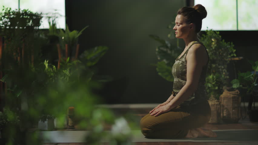 modern middle aged housewife with yoga mat stretching at modern green home.