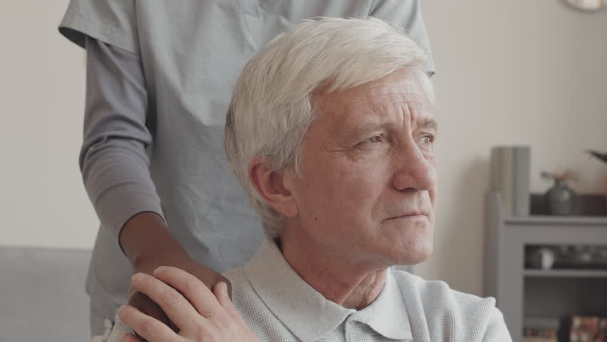 Medium closeup with slowmo of unrecognizable nurse placing her hand on shoulder of sad Caucasian senior man looking straight forward and trying not to cry | Shutterstock HD Video #1098889077